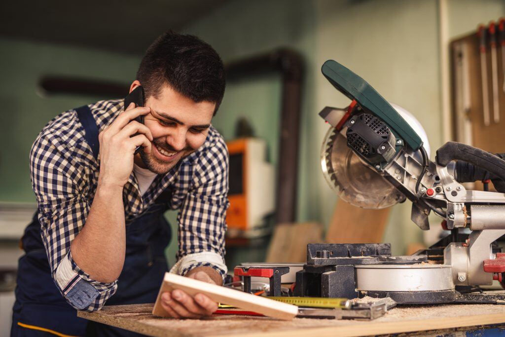 Ein glücklicher junger Handwerker am Telefon - Mit den passenden CRM Prozessen wird Kundenzufriedenheit ein Kinderspiel