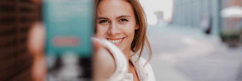 EInes Frau zeigt fröhlich Ihr Handy in die Kamera - Nutzen auch Sie zur Mitarbeitergewinnung Social Media