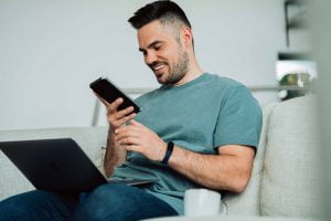 Ein Mann schaut lächelnd auf sein Smartphone - Video SEO hilft Ihrem Unternehmen sichtbar zu werden