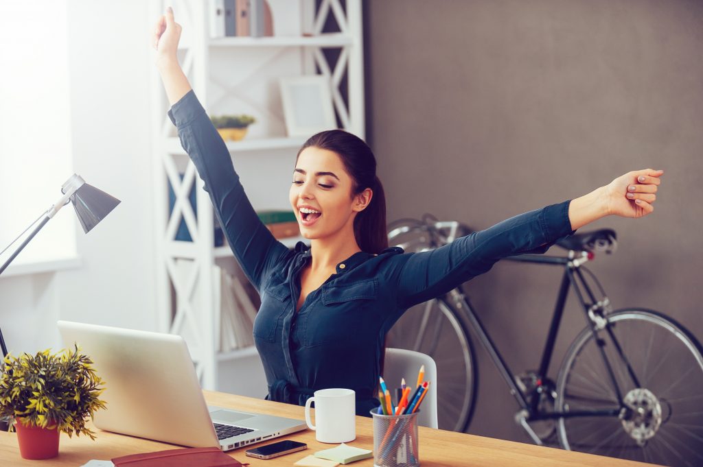 Eine Frau im Business Outfit sitzt vor dem Laptop und freut sich - Starten Sie mit Linkedin Marketing heute und gewinnen Sie Ihre ersten Kunden und Mitarbeiter.
